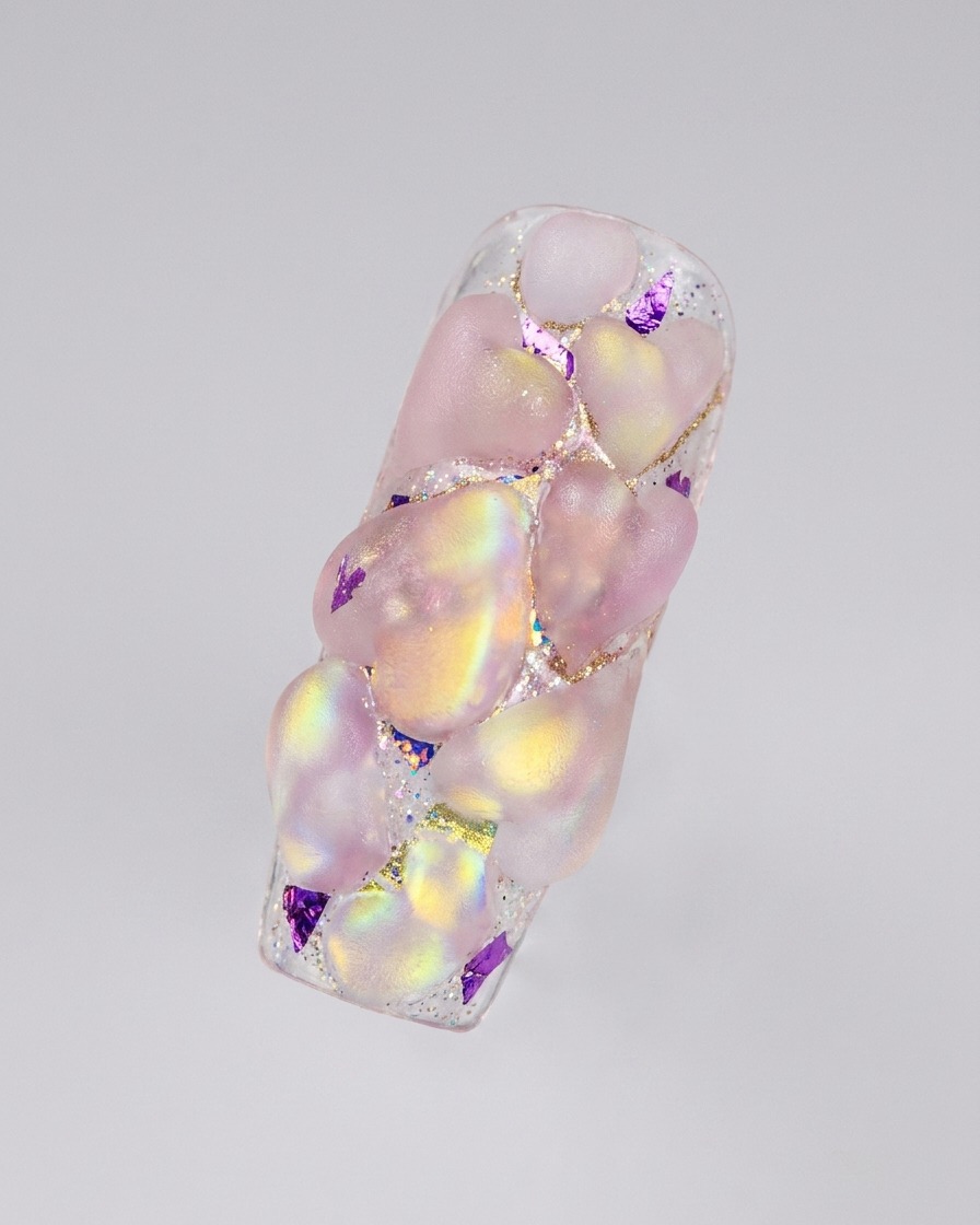 A completed layout of multiple 3D iridescent acrylic hearts covering an elongated nail surface.