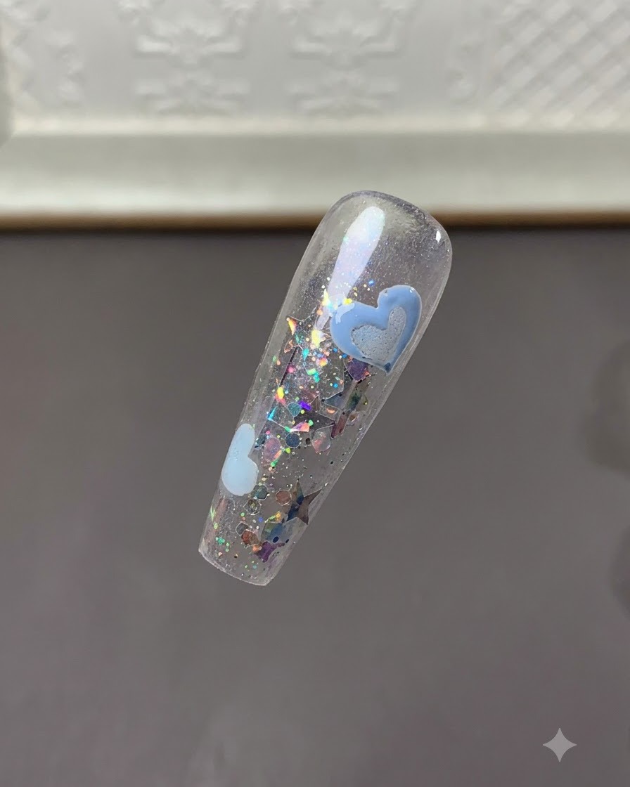 A clear view of the nail tip showing cured light blue heart designs amidst glitter flakes.