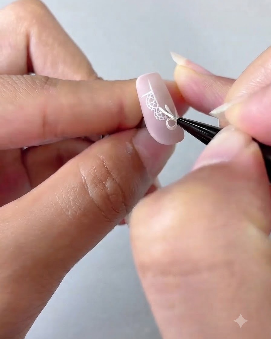 A nail art brush adding detailed white dots and a four-pointed star onto a pink gradient nail.