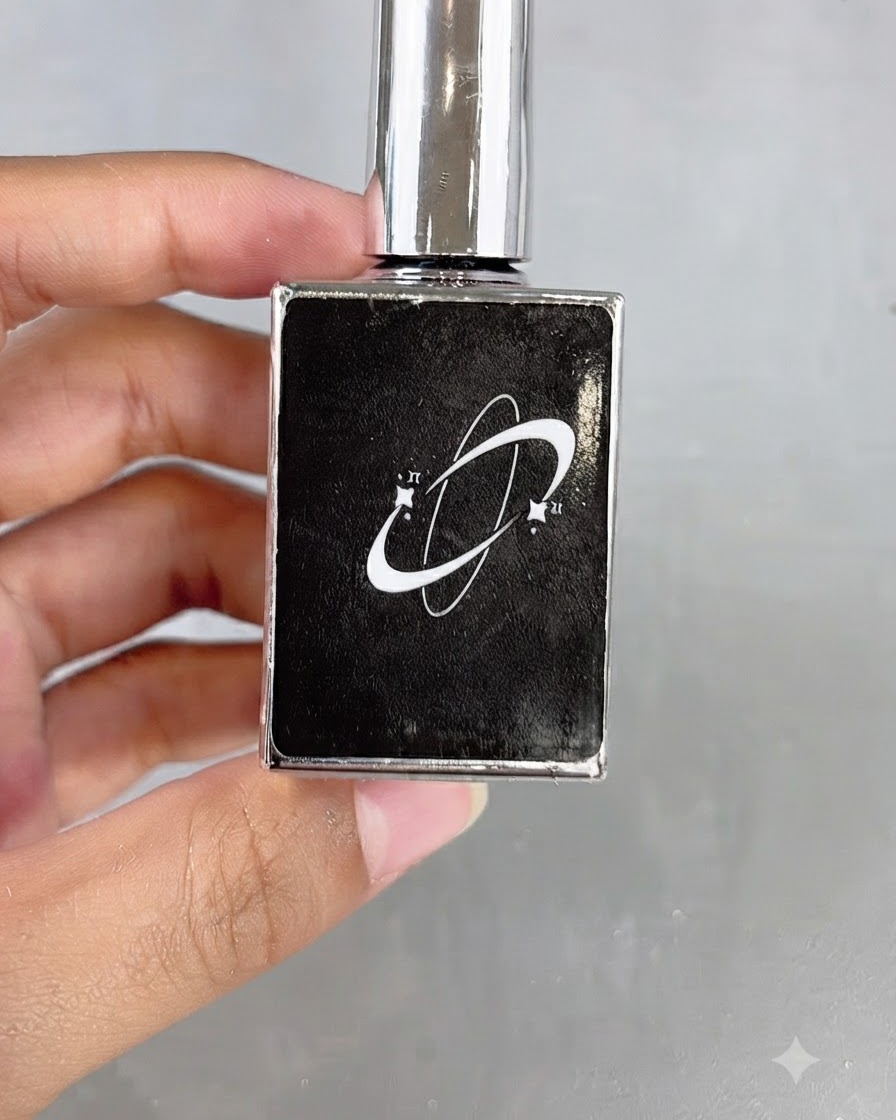A black cosmetics bottle featuring a planet logo graphic being held in hand.