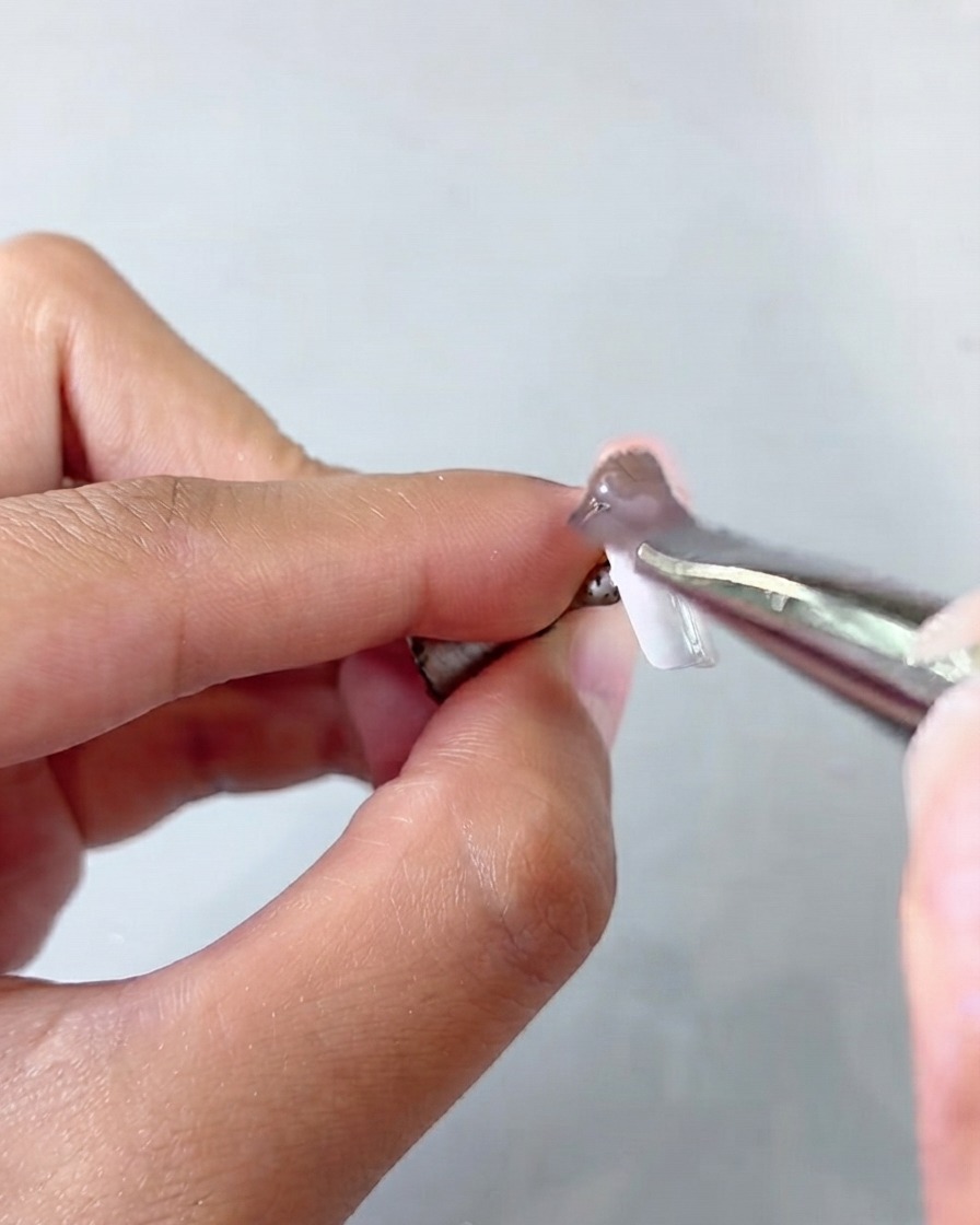 A pair of tweezers holding a nail tip while applying a cat eye gel layer.