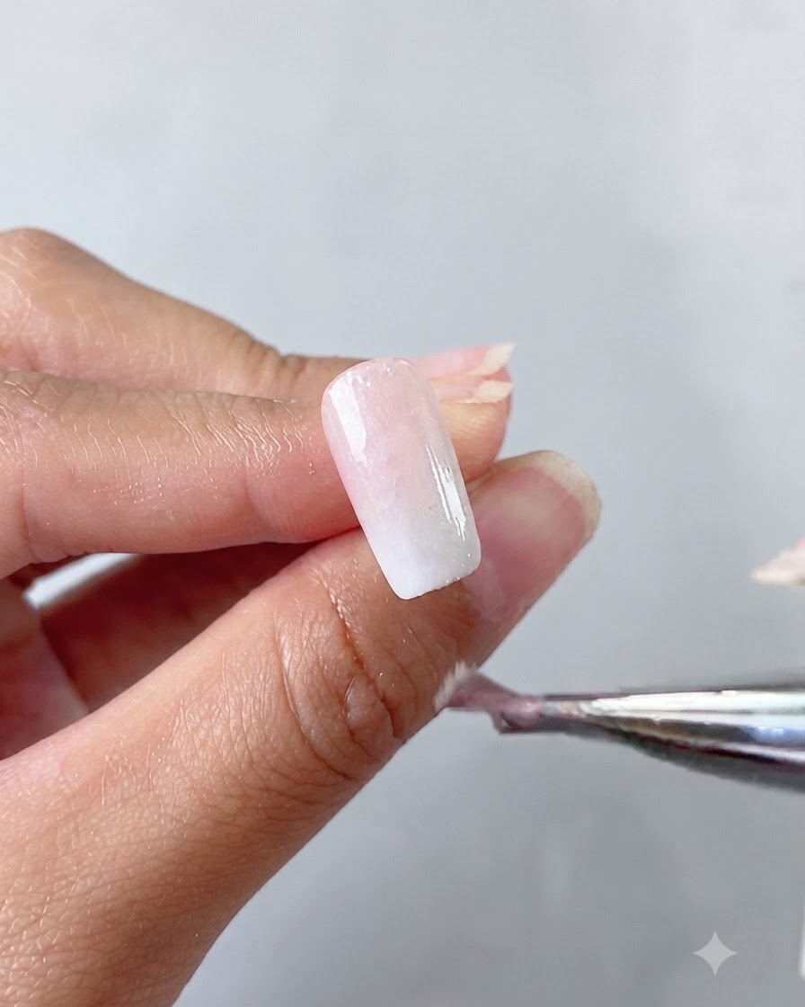 A hand holding a brush applying a milky white cat eye gel base coat onto a nail.