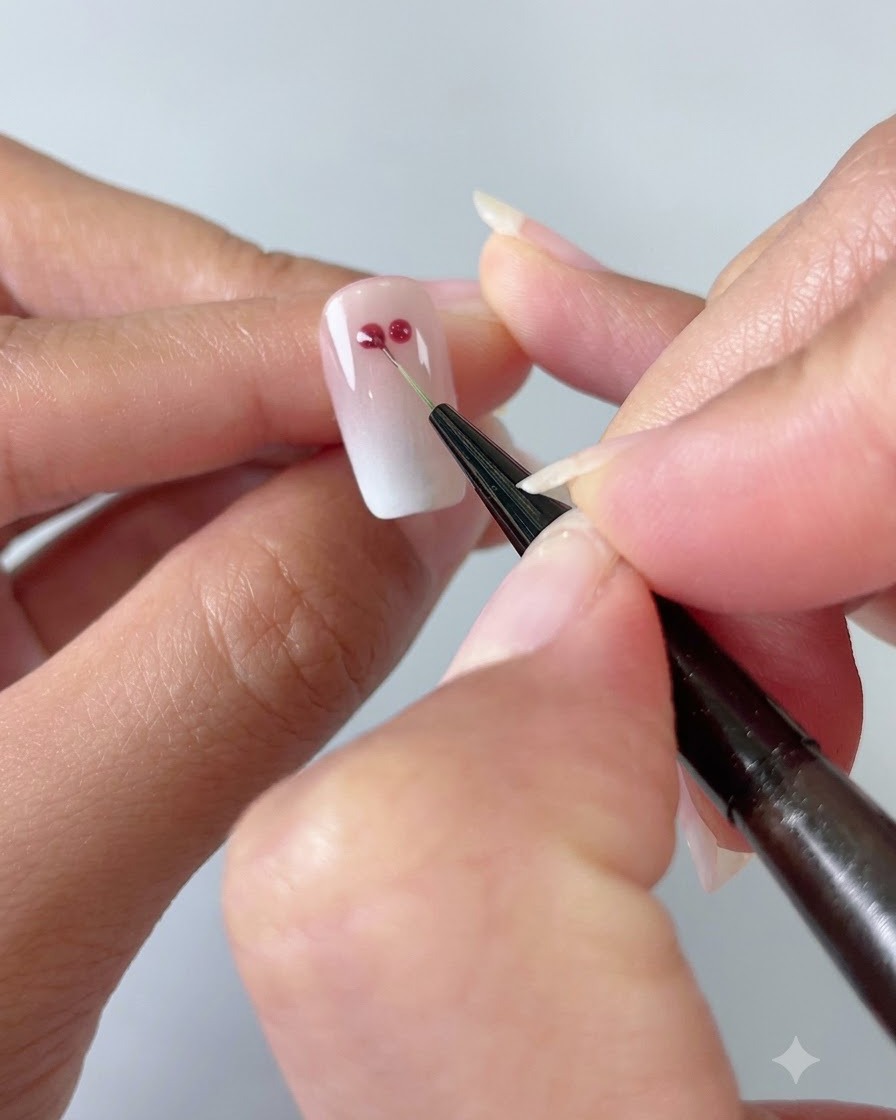 A fine nail art brush connecting two red gel dots into a heart shape on a gradient cat-eye nail.