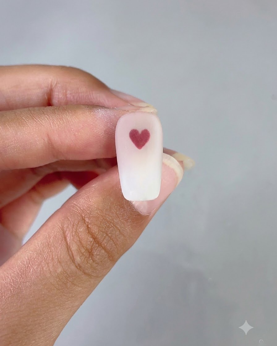A finished nail showing a neat pink and white gradient background with a clean red heart in the center.