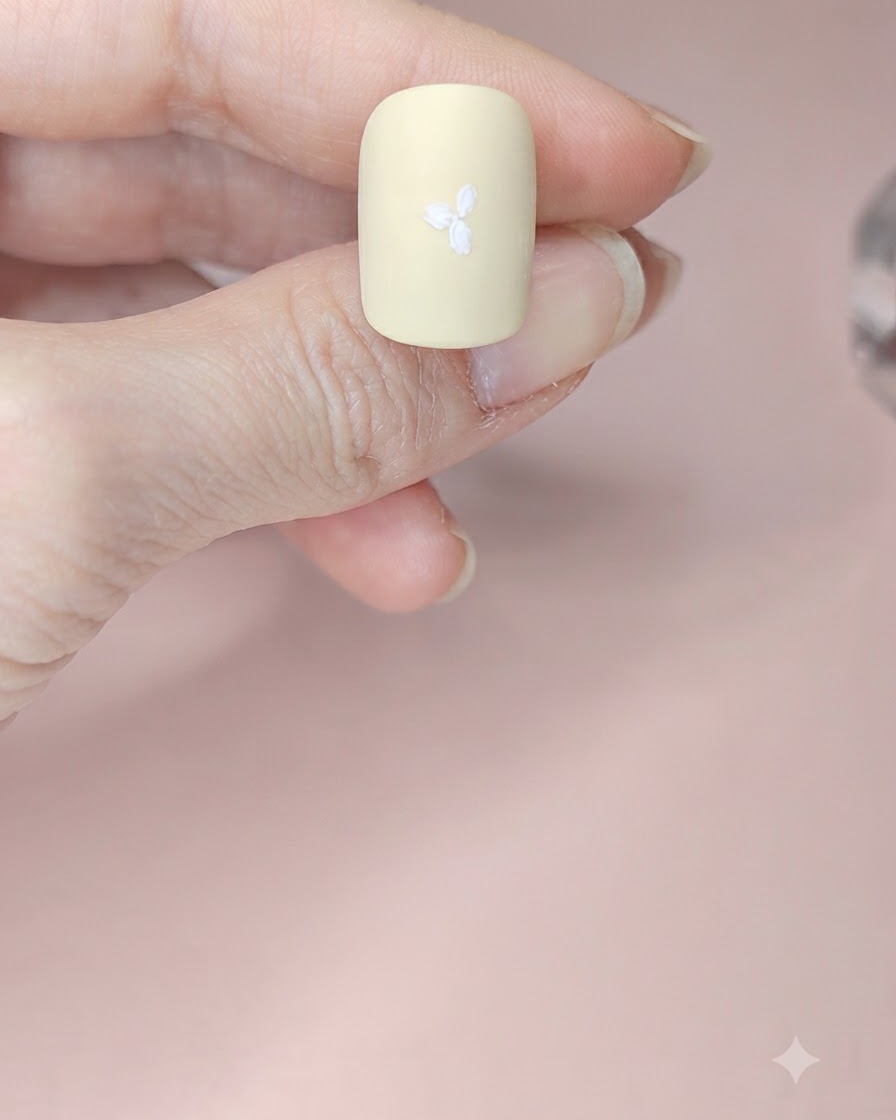 A pale yellow nail with three white flowers painted across the surface.