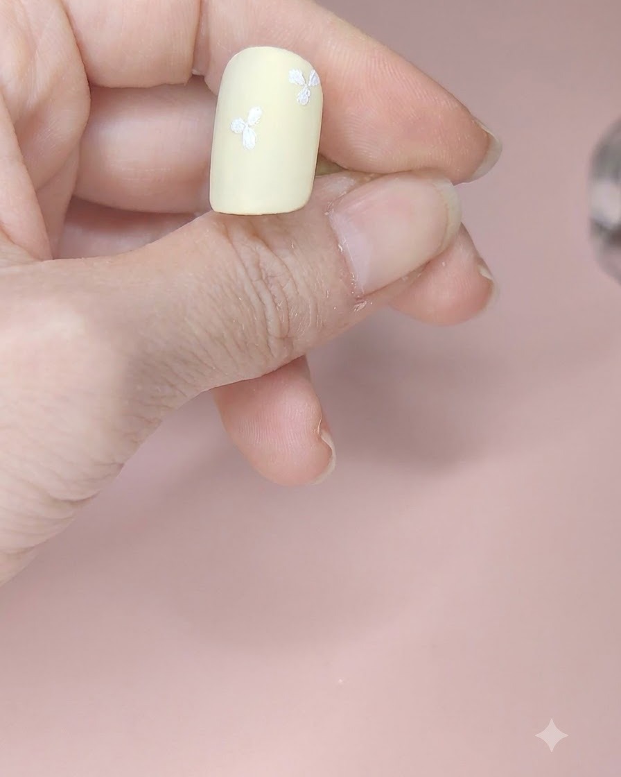 A pale yellow nail featuring four white three-petal flowers arranged across different areas.