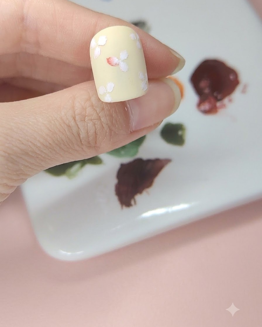 A pale yellow nail with white flowers where the center of the middle flower is tinted with red watercolor.