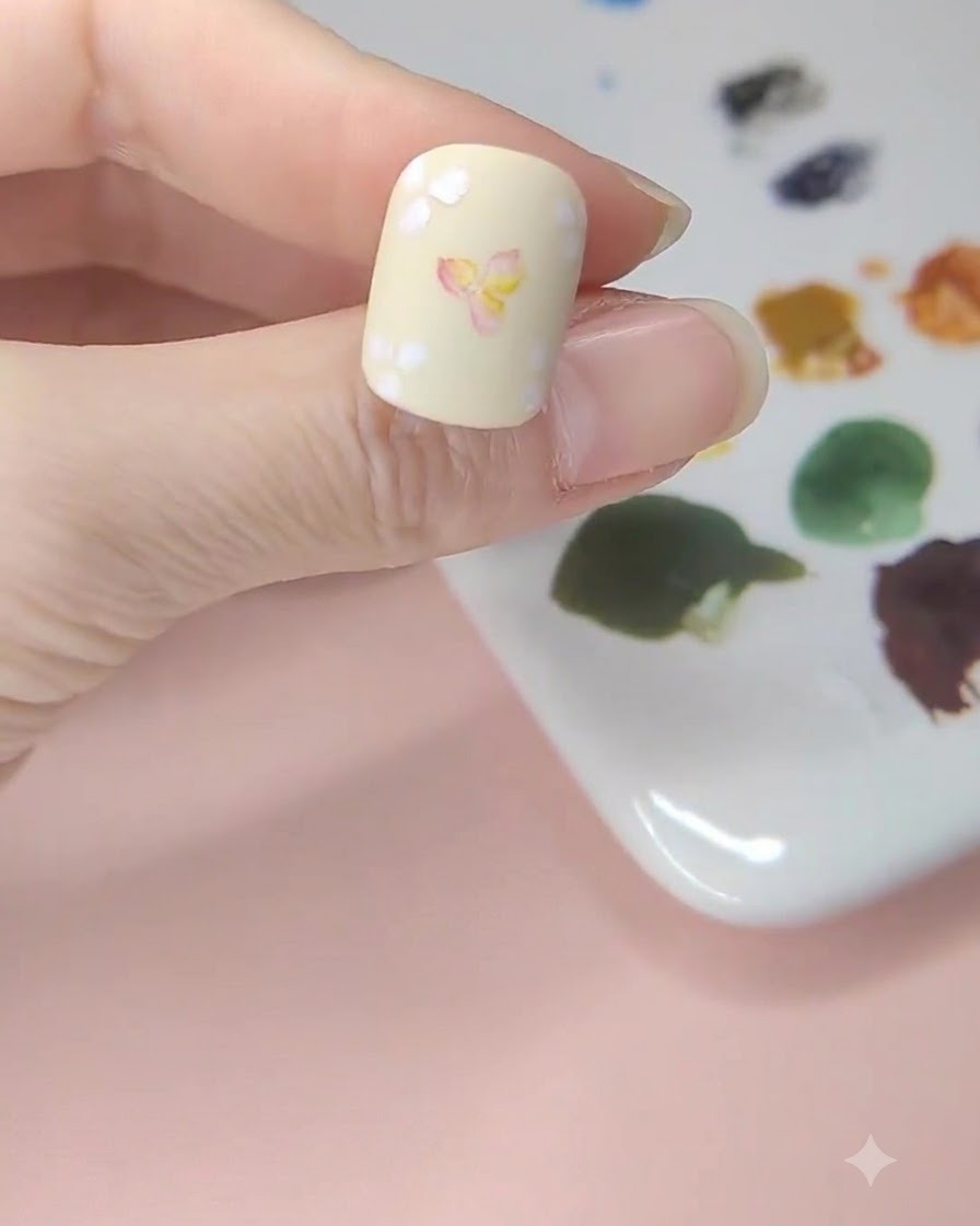 A pale yellow nail showing yellow watercolor washes applied to the blank spaces around the floral art.
