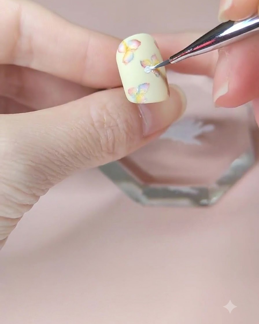 A detailed close-up of a fine nail art brush adding a second layer of white petals to the center flower.