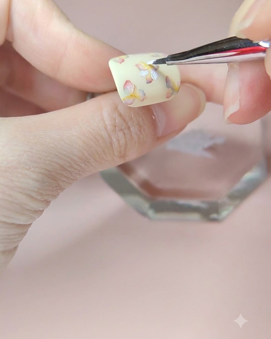 A fine brush applying a second layer of white petals onto the top left flower of the nail.