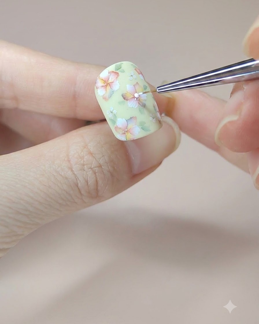 A fine brush adding the final white dots into the flower centers on a decorated yellow nail.