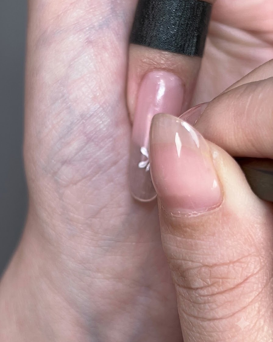 A close-up of a white painted flower forming on the nail surface.