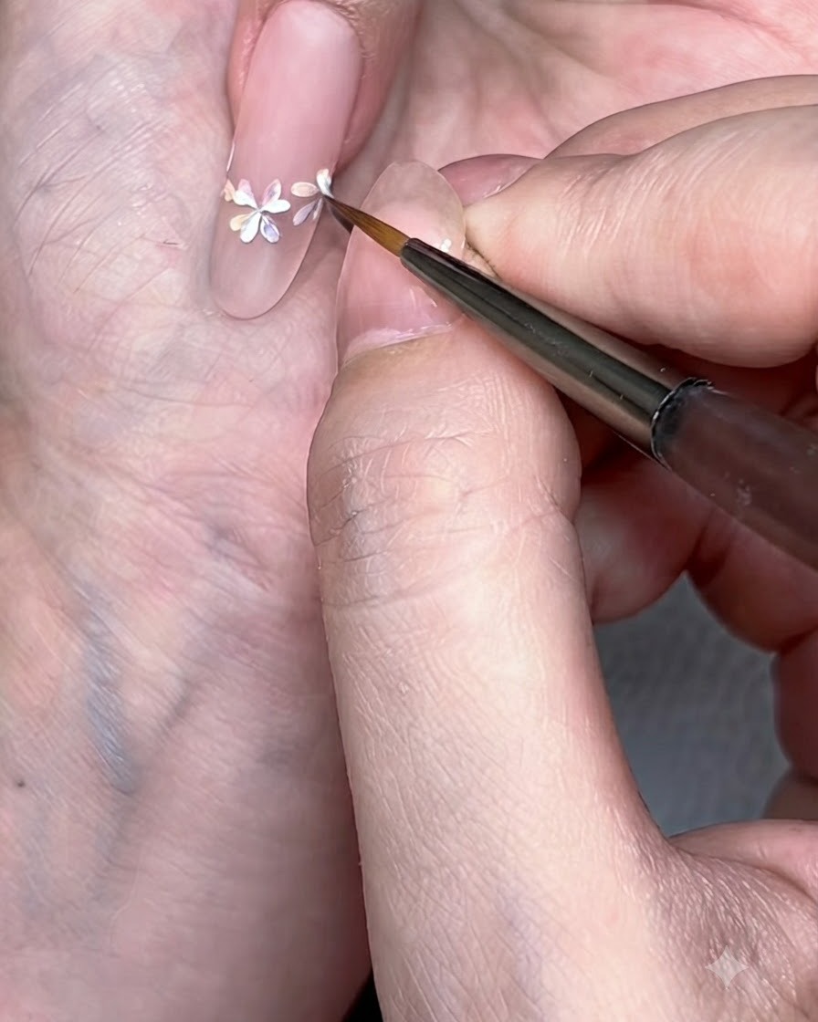 A detailed close-up of a liner brush adding crisp white petals over the watercolor flower centers.