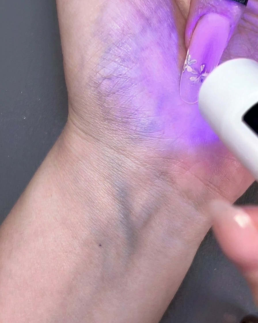 A handheld mini UV lamp curing a floral nail design under a purple light.