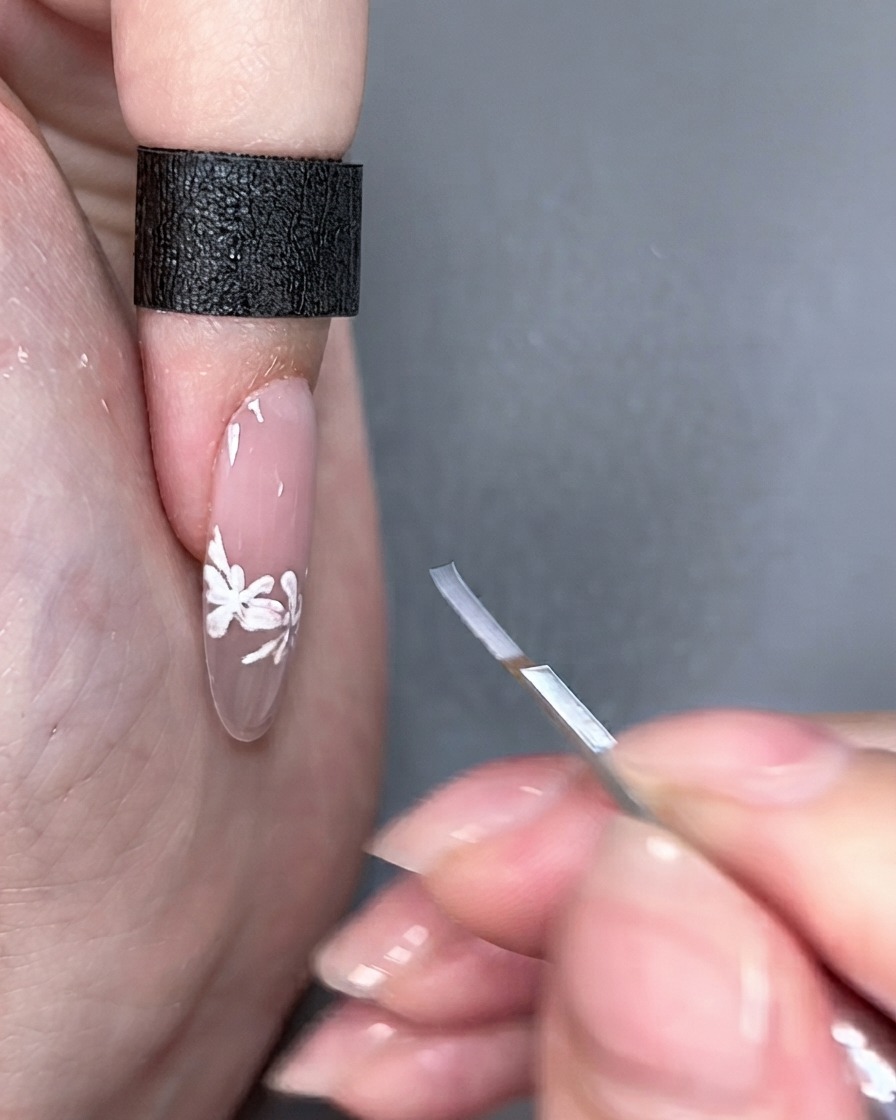 A nail art brush held next to a finished fingernail under studio lighting.