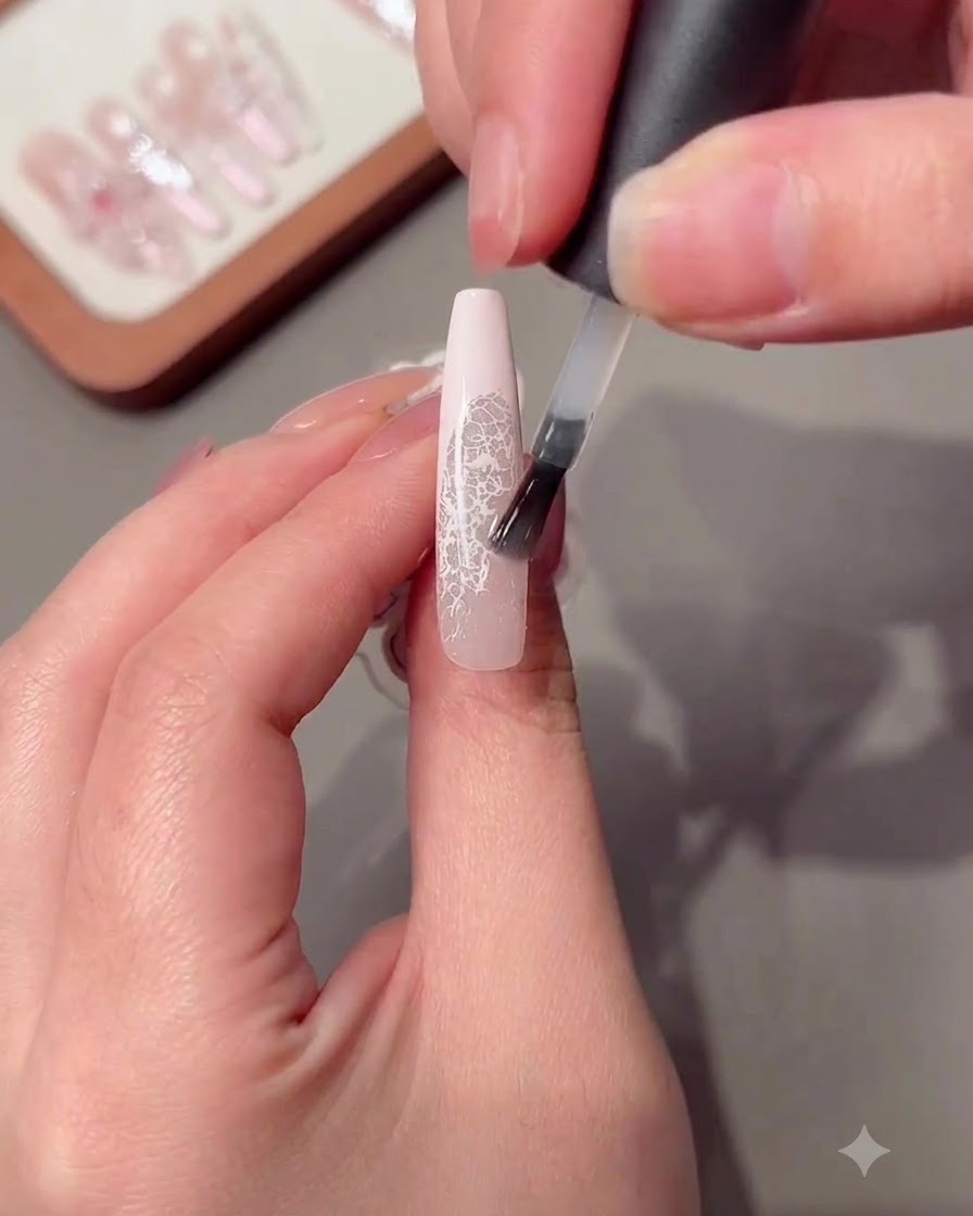 A brush applying a clear reinforcing gel layer onto a long manicured nail.