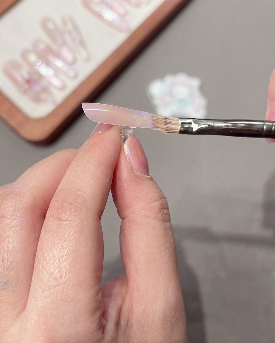 A brush gently sweeping across the nail surface to blend a smooth color gradient.