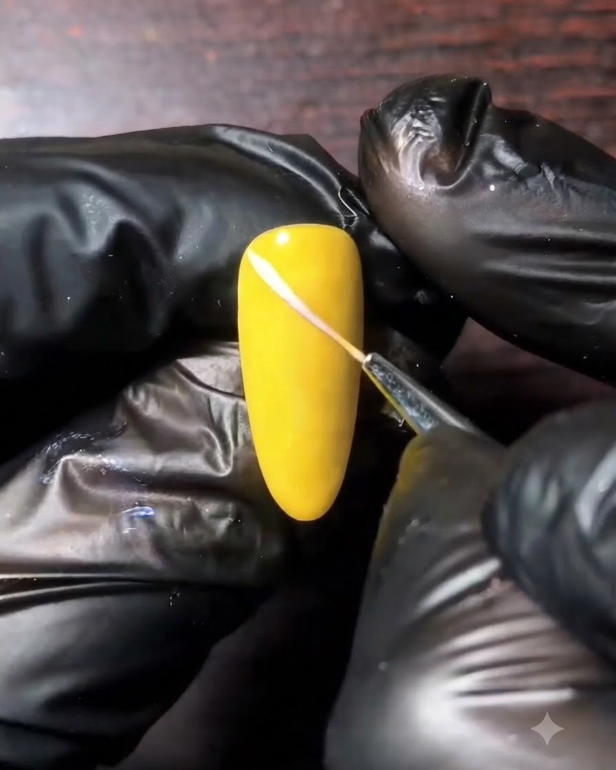 A fine liner brush drawing a white diagonal line across a yellow nail surface.