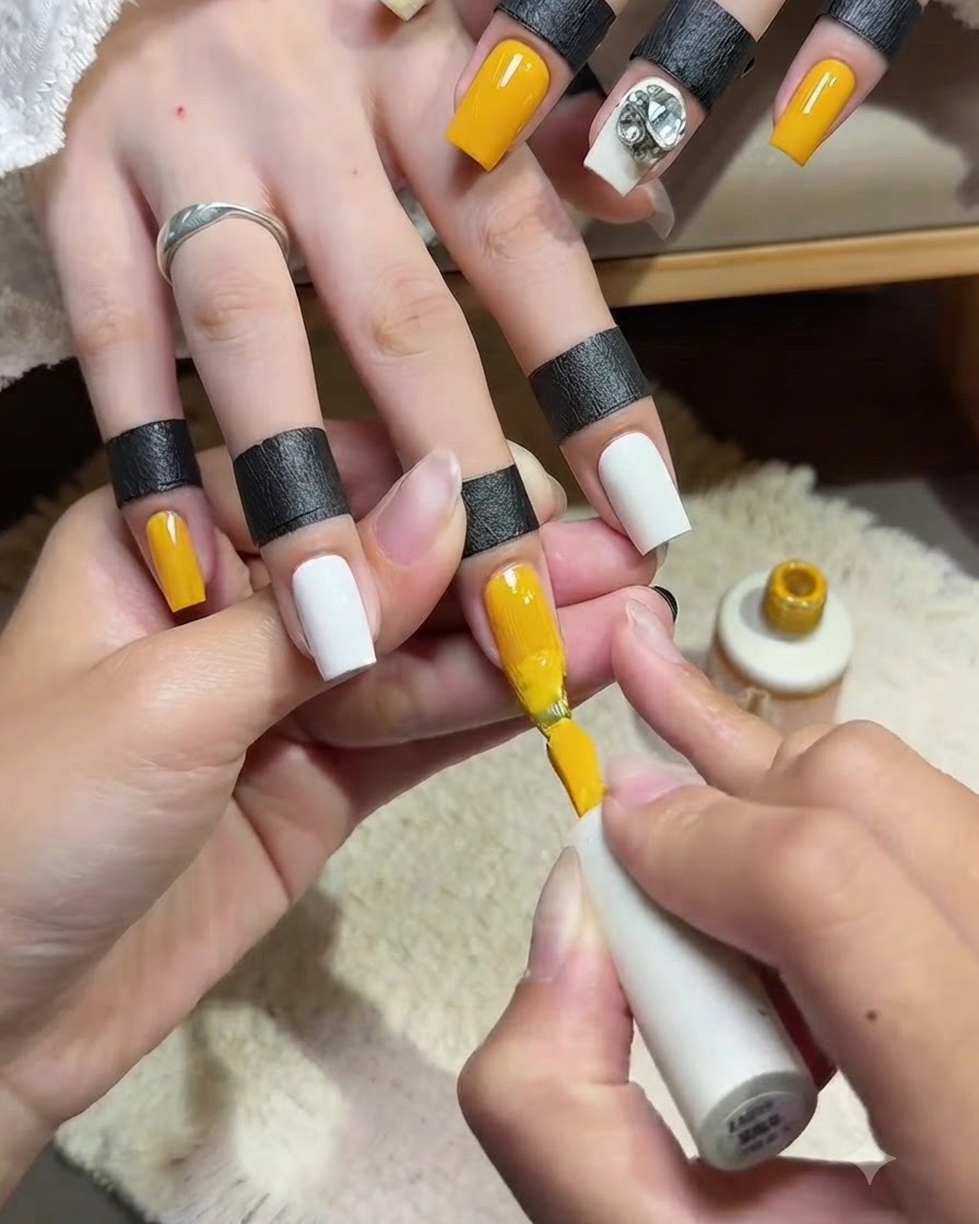 A close-up of a nail technician applying a smooth second coat of bright yellow gel polish onto an index fingernail with the polish brush.