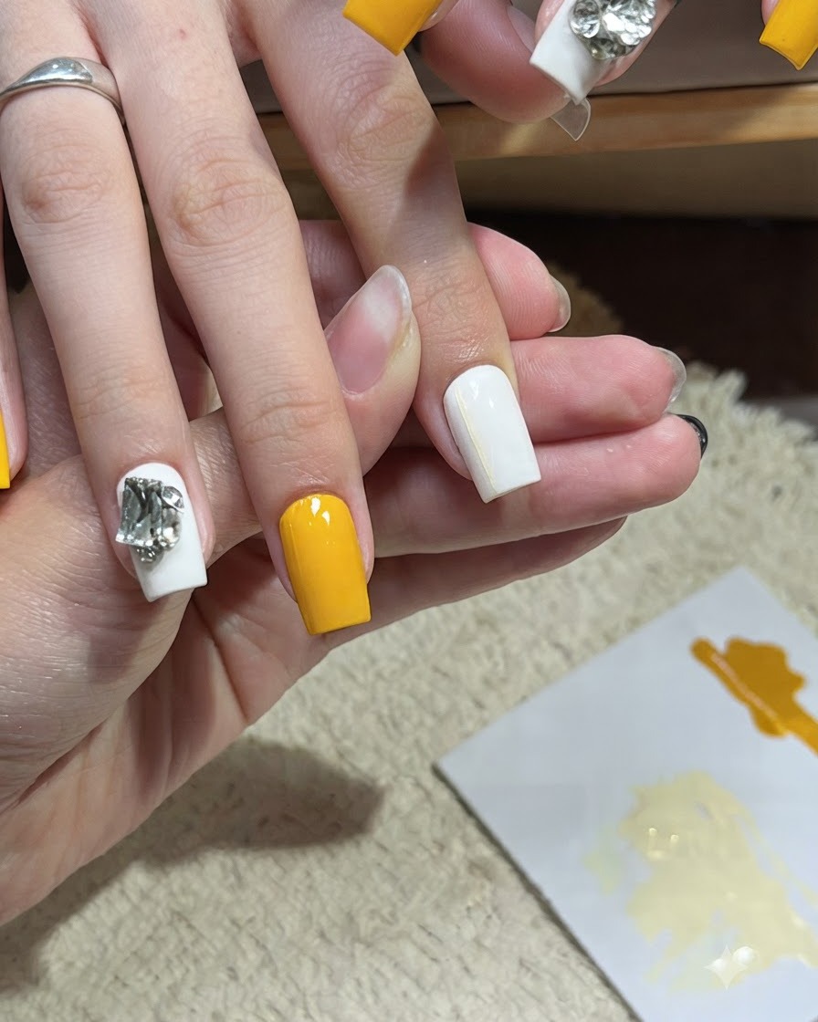 A nail art brush applying a second thin horizontal yellow line onto a white nail.