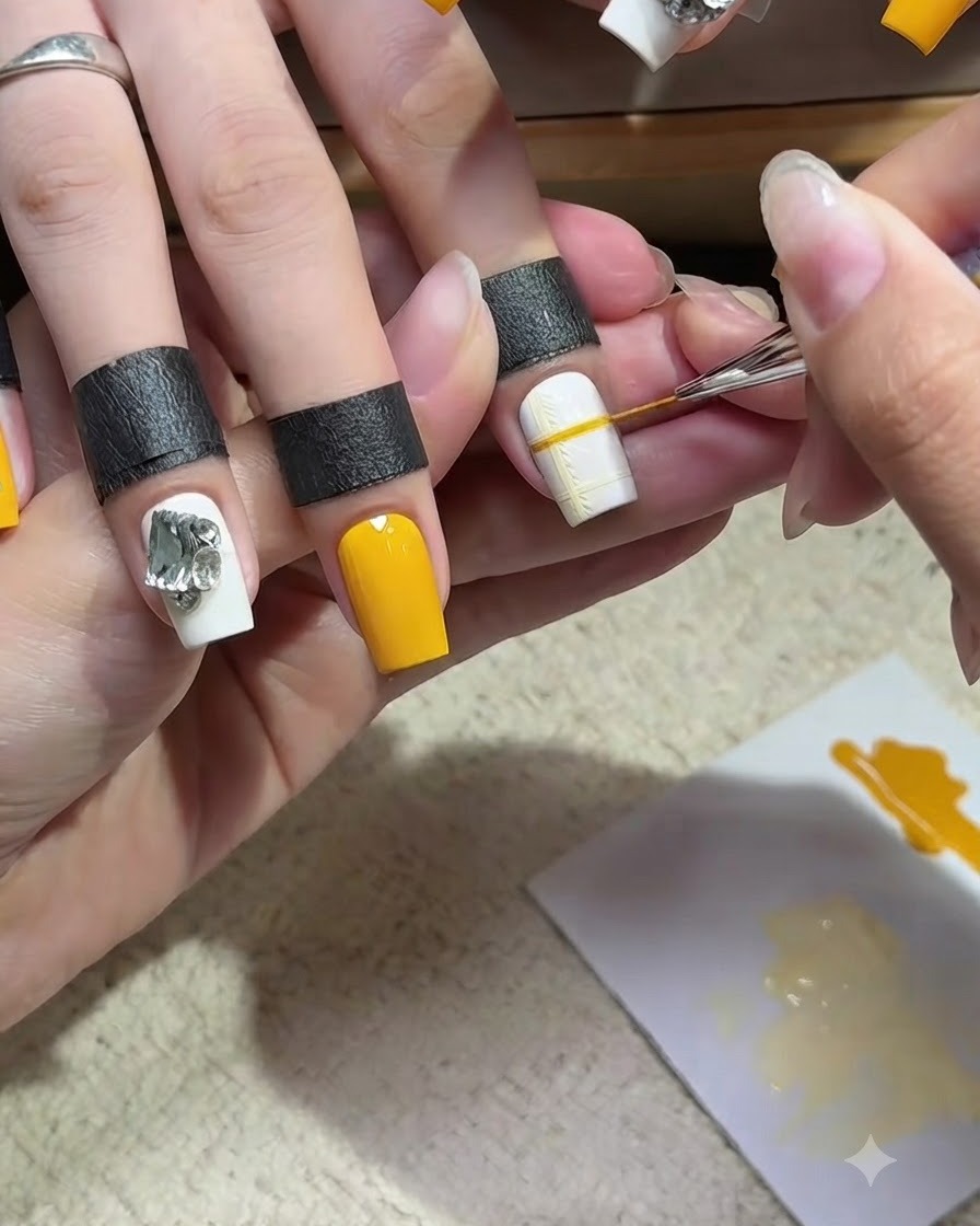 A fine liner brush drawing a yellow intersecting line over a white nail base, completing a delicate yellow plaid grid pattern.