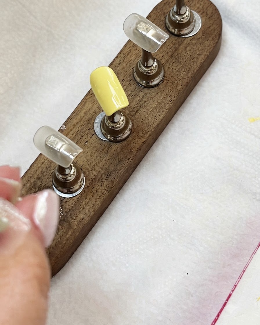 Nail tips on a wooden stand showing a milky yellow tip and nude colored tips.