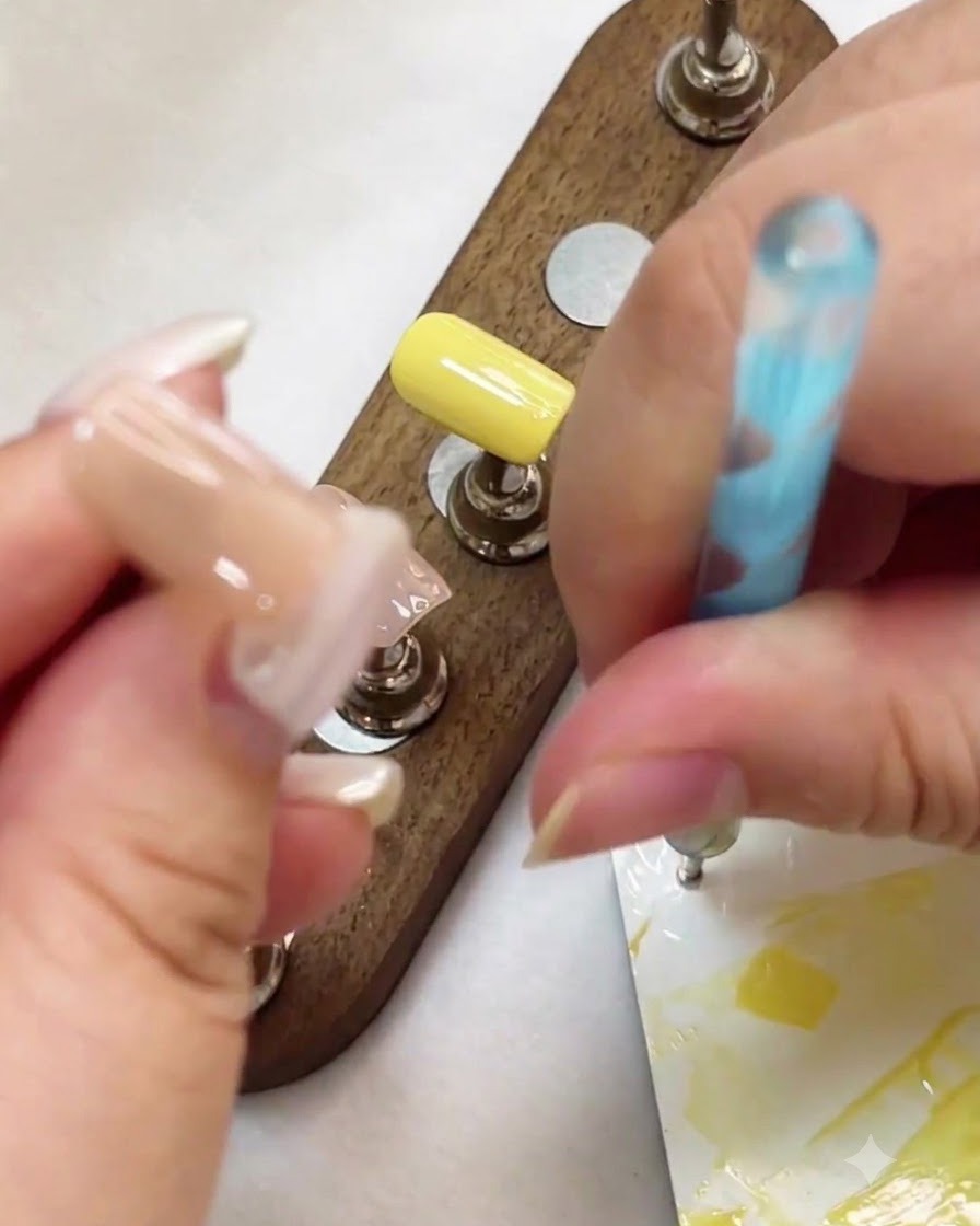 A dotting pen being used to place white gel dots on a nude nail surface.
