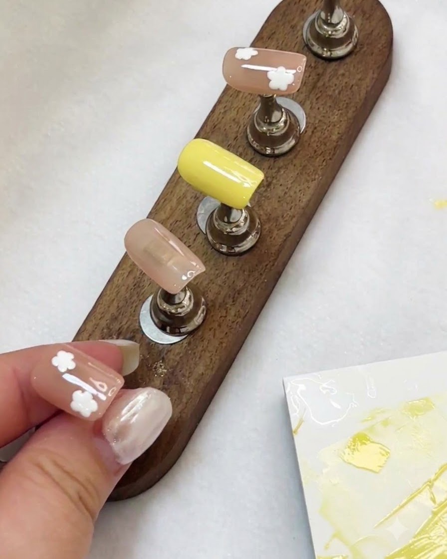 A display stand holding multiple painted press-on nails with white flower designs under lighting.