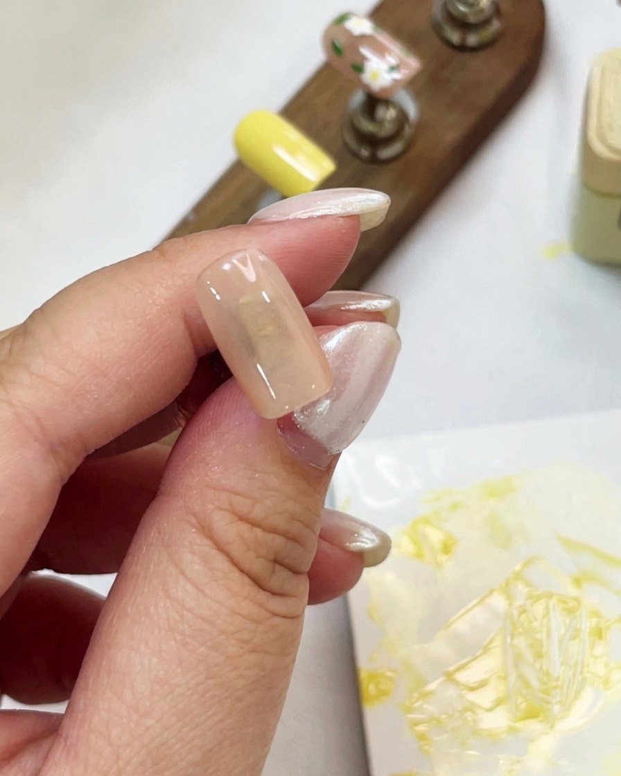 A close-up of a hand holding a nude-colored nail tip while applying shimmering cat-eye gel with a brush.
