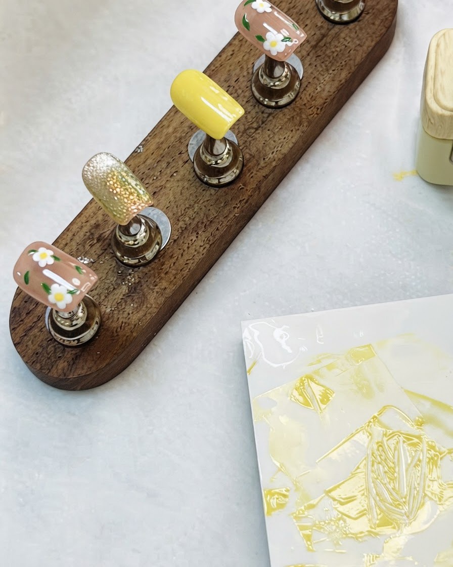 A wooden display stand holding completed floral and cat-eye nail art tips on a table.