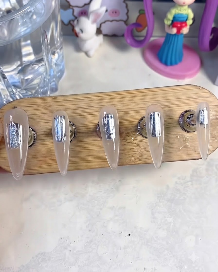 A nail stand with five fake nails placed inside a UV/LED curing lamp to cure the base gel layer.