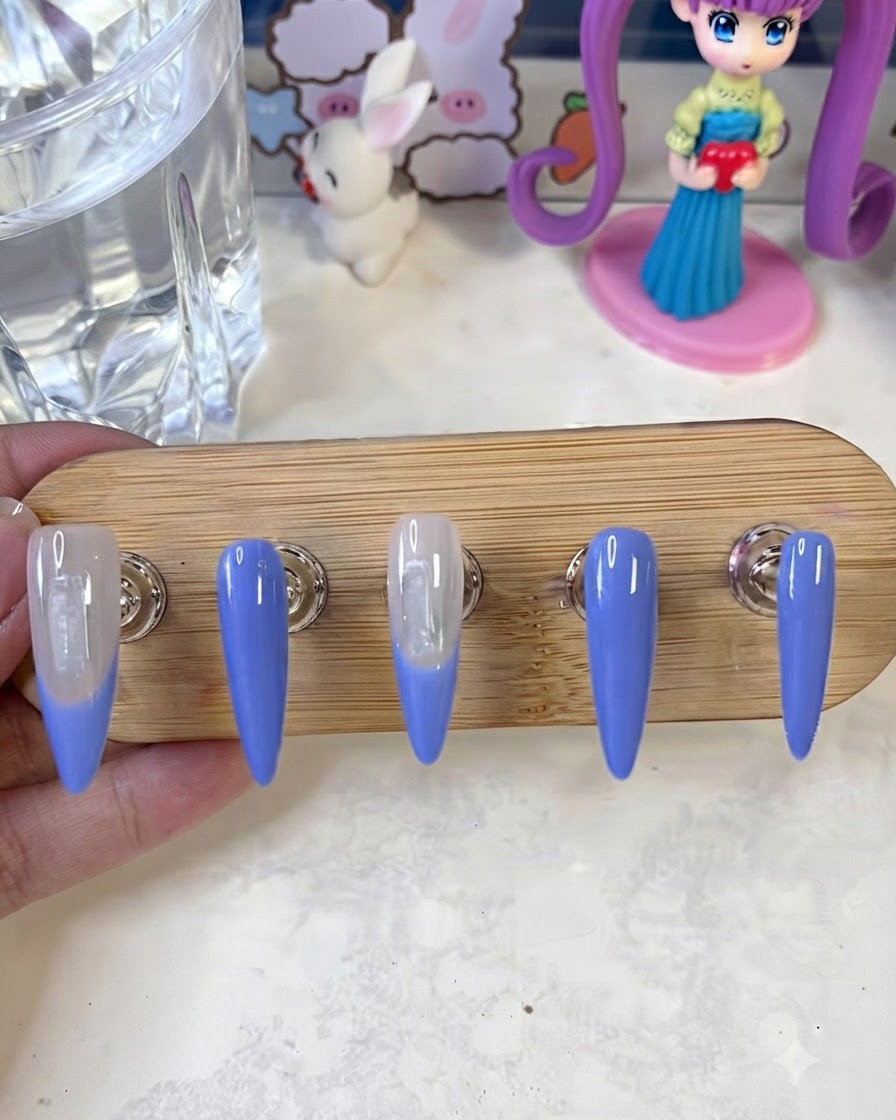 Nail art brush applying a second layer of blue French tip paint to the nail edges on a display stand.