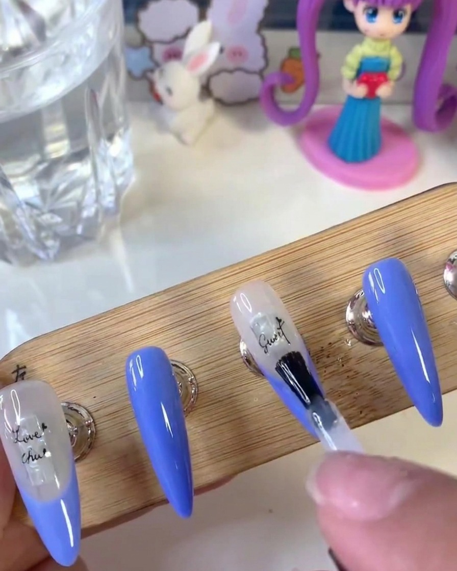 A nail brush applying a clear layer of reinforcement gel over a nail surface with letter stickers.