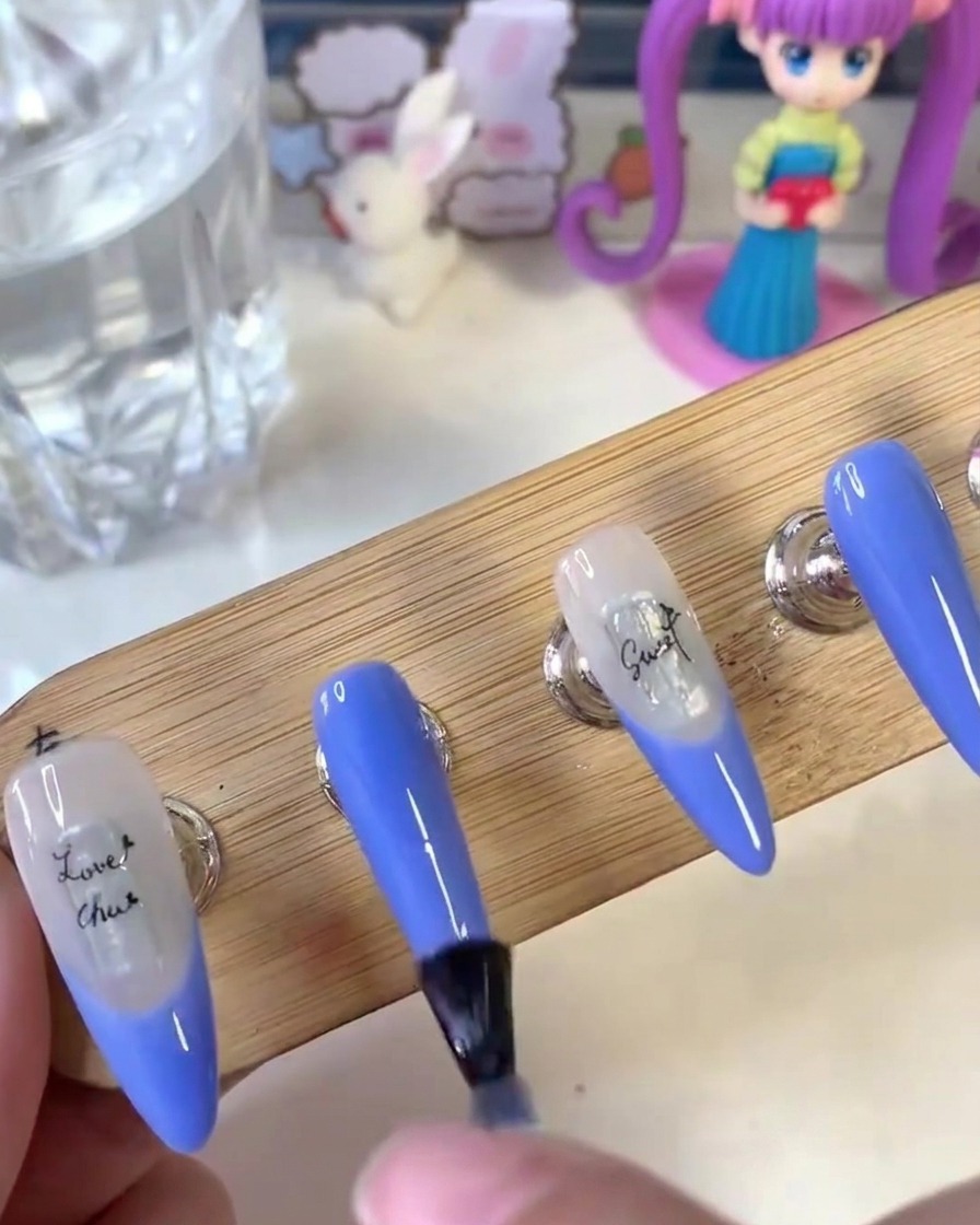 A brush applying matte top coat uniformly across the surface of the painted nails on a wooden stand.