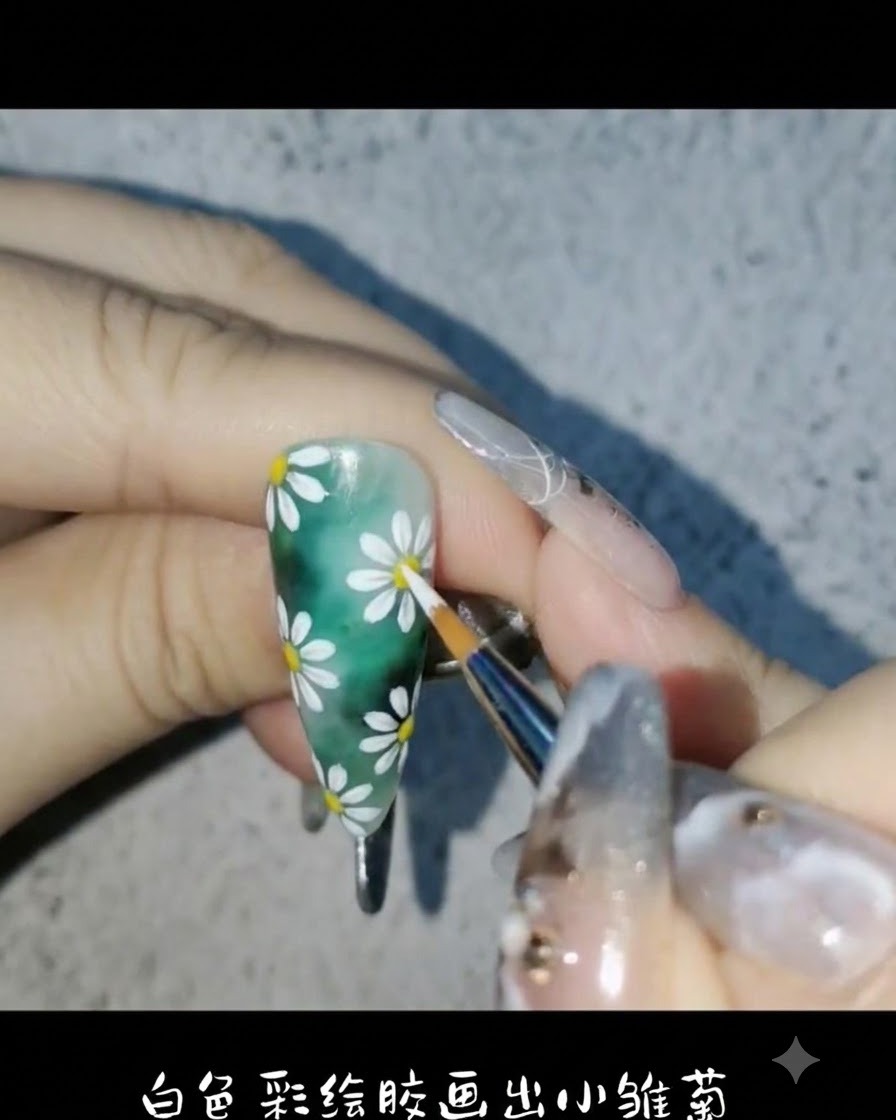A liner brush using white painting gel to draw delicate daisy petals on the green nail backgroundcite: 1.