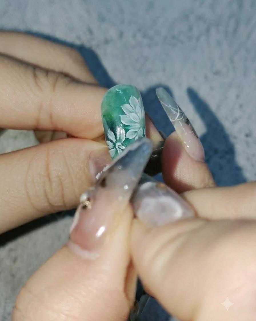 A close-up view of a nail artist adding deeper white petals to daisies on a green nail design.