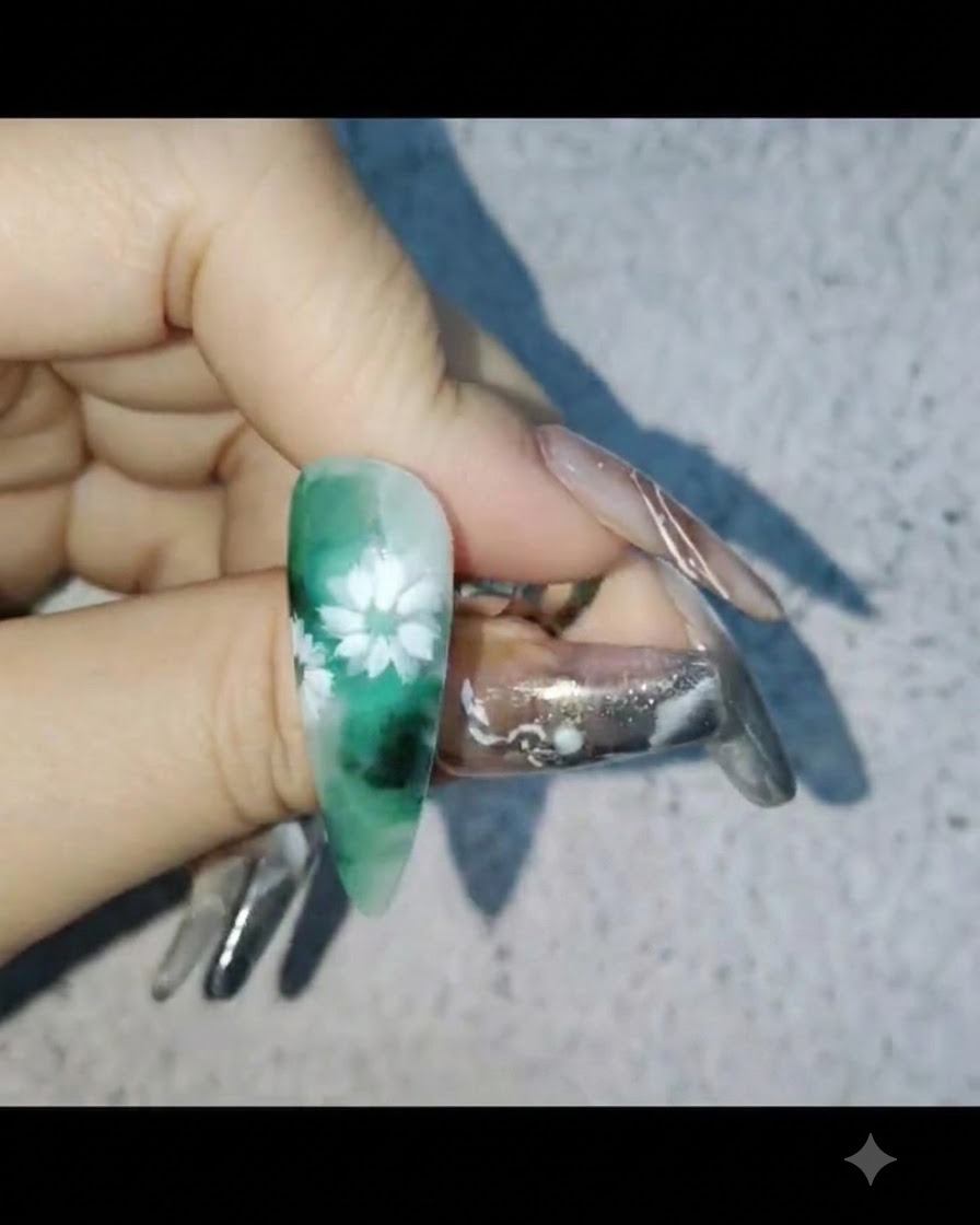 A hand holding a nail with white daisy nail art while applying a protective layer of reinforcing gel.