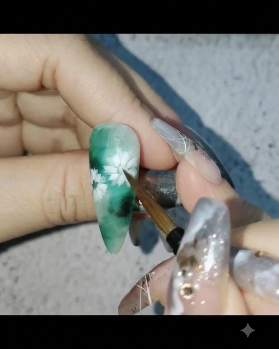 A nail brush applying matte top coat over a green-themed floral nail design.