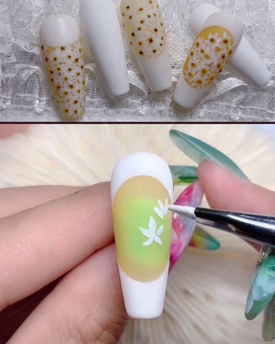 A fine brush painting white daisy petal shapes onto the yellow-toned nail.