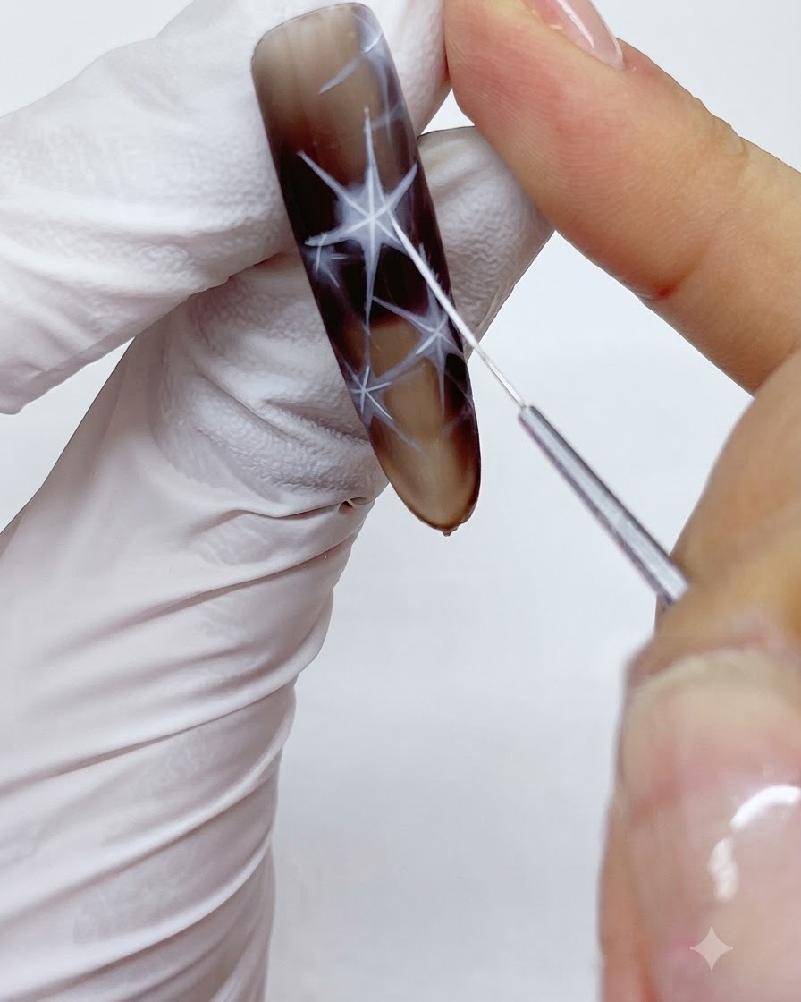 A fine liner brush carefully tracing and outlining the outer borders of a white starburst design on a nail.