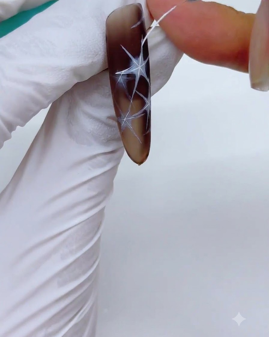 A nail with outlined white starburst designs being placed into a UV/LED lamp to cure.