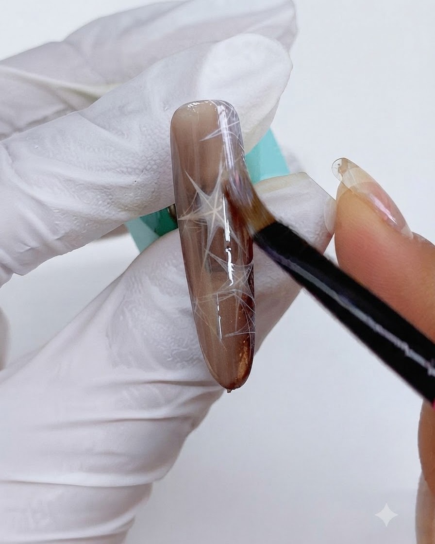 A fine brush applying cat eye gel over the decorated brown nail.
