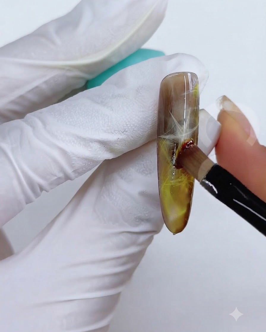 A brush and sponge technique being used to blend the yellow-brown color on the nail surface.
