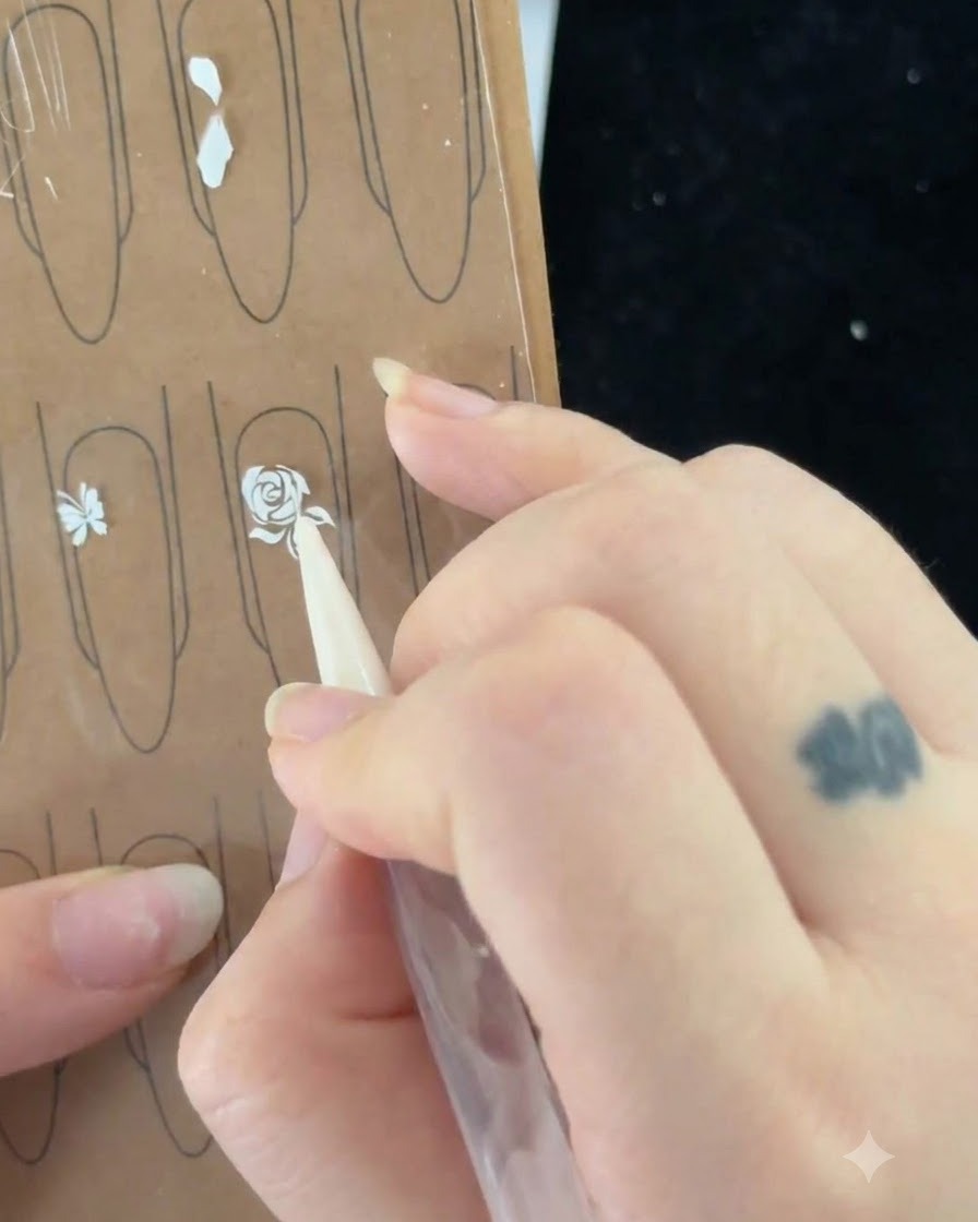 A nail brush pulling a thin line to start painting a leaf next to the rose.