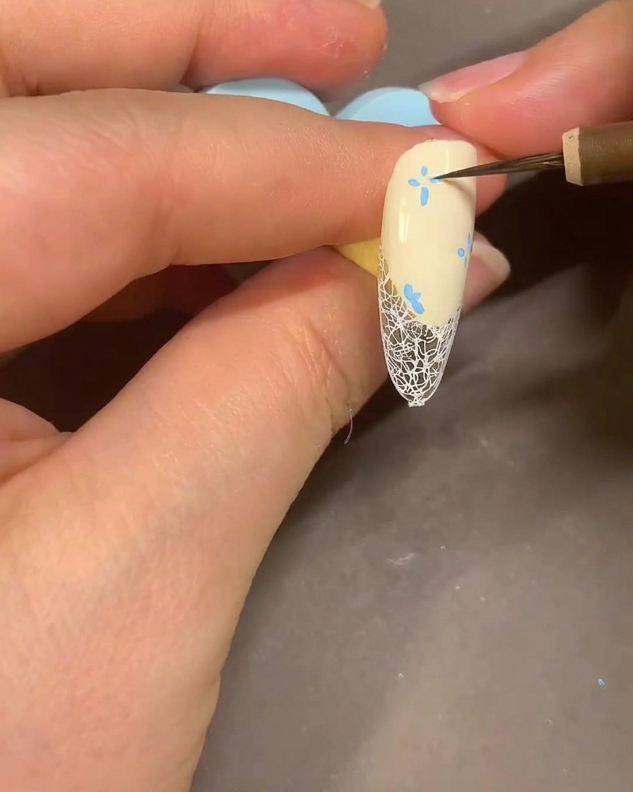 A watercolor brush blending blue marker flower petals on a nail with alcohol for a smoky look.