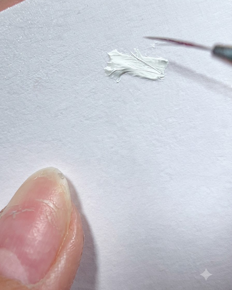 A fine liner brush picking up white gel paint from a white surface palette.