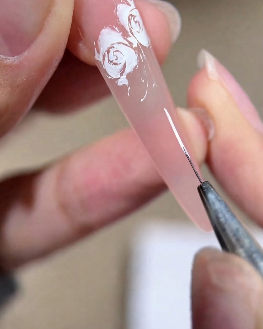 A close-up view of a nail technician drawing a white parenthesis shape on a pink nail plate.