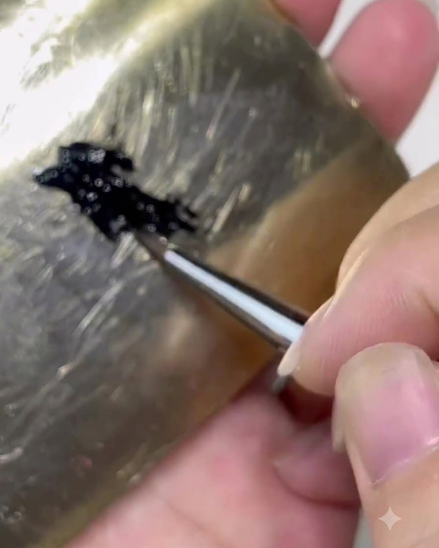 A brush loading black gel product from a palette onto roughly one-third of the brush body.