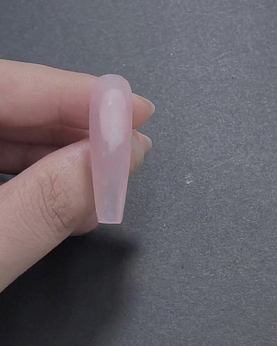A close-up of a long coffin-shaped nail painted with a smooth, glossy sheer pink gel base coat being held between fingers.