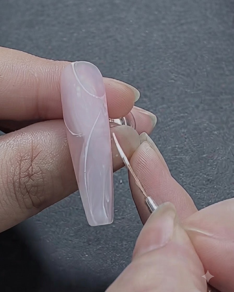 A fine brush outlining the initial curved white strokes of a rose pattern on the upper section of the nail.